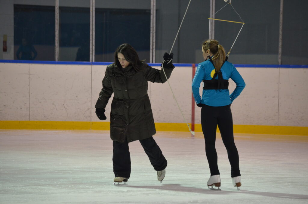 Coach Jo-Ann on the ice with a skater in stirrups